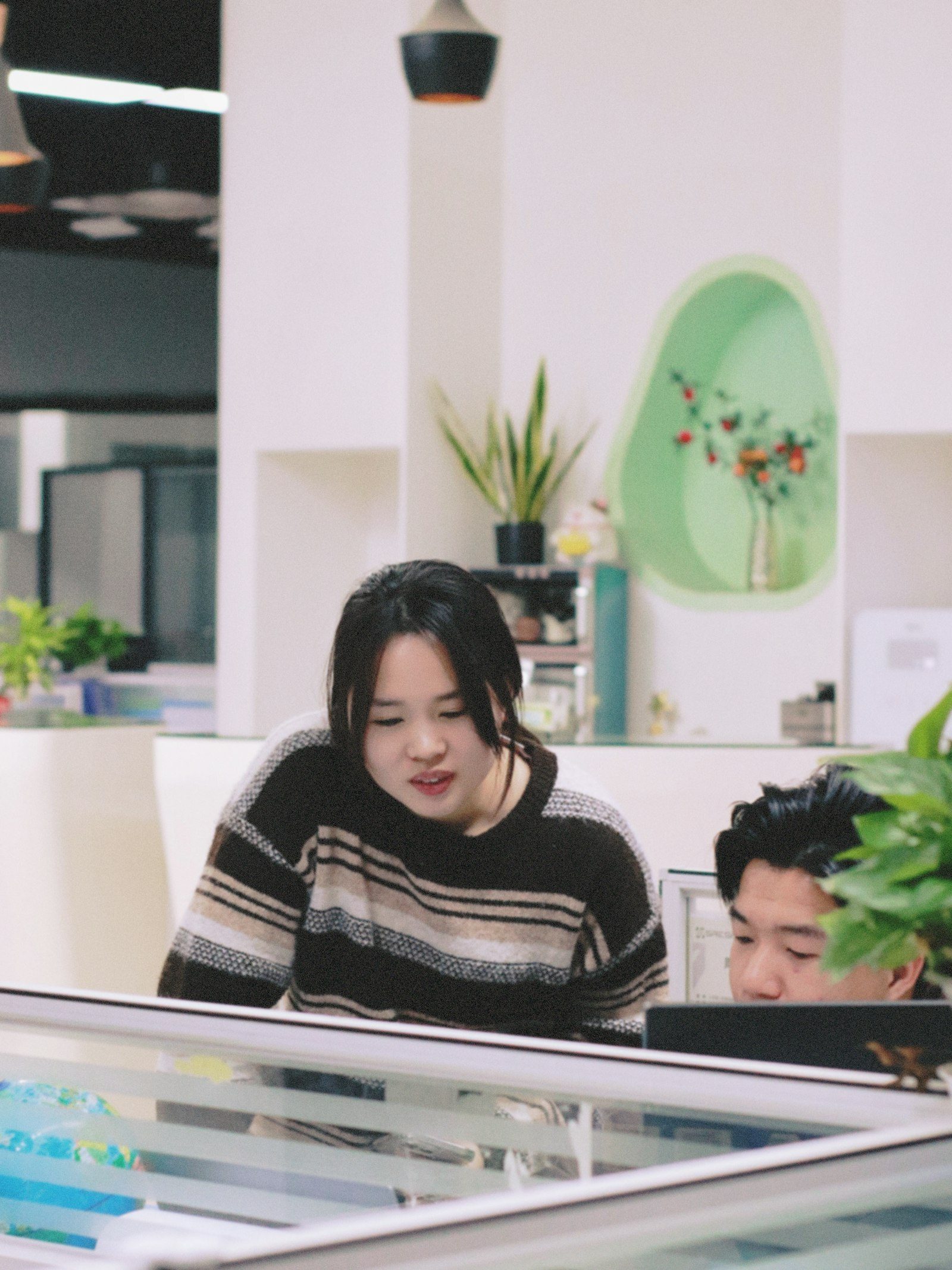 Colleagues work closely at computers in a sunlit brick-walled studio office.